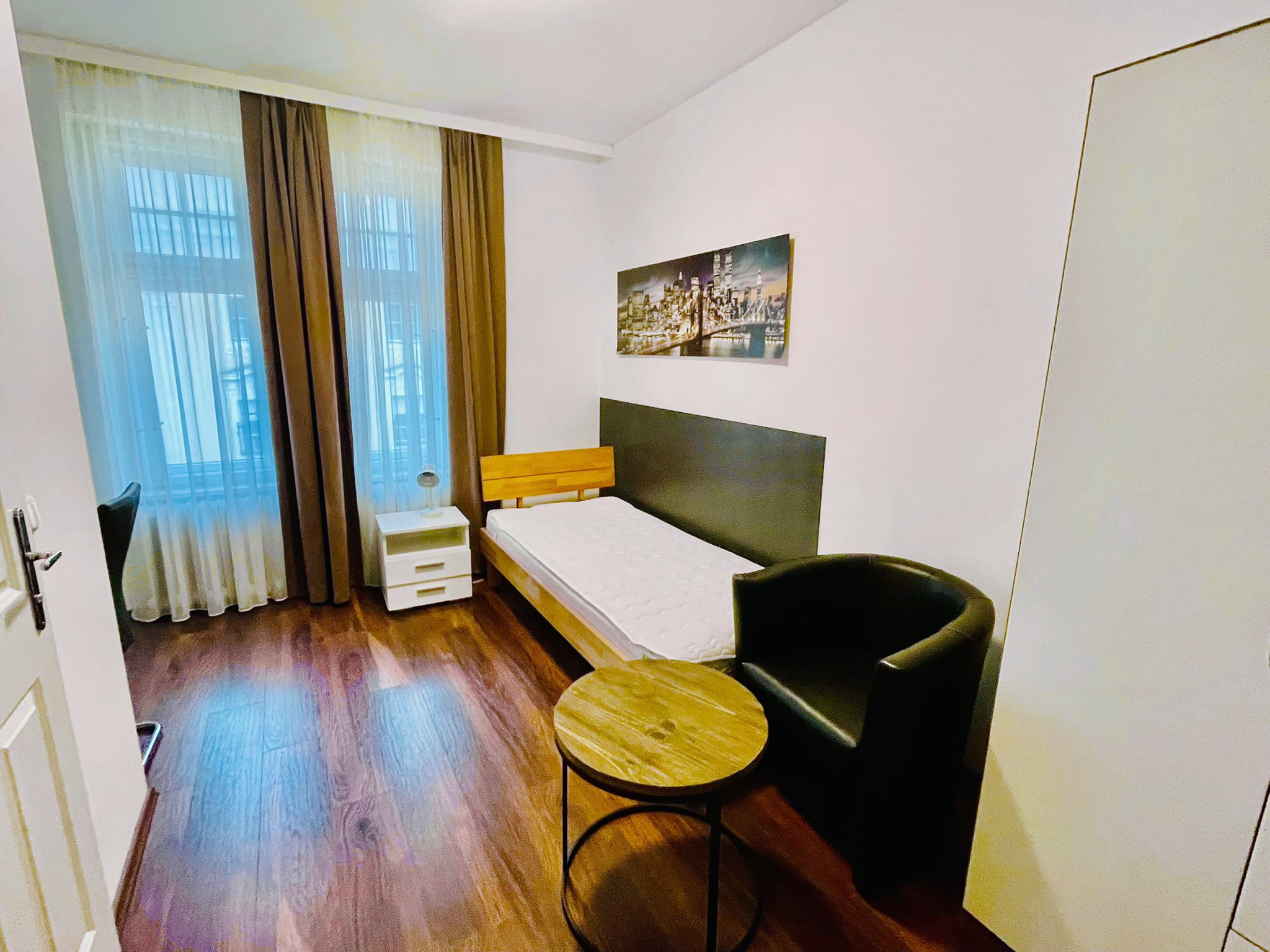 Einzelzimmer mit Bett, Sitzplatz und großen Fenstern
